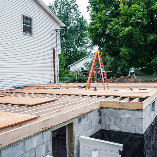 Home addition in early stages with foundation laid and flooring boards being installed on the first floor.