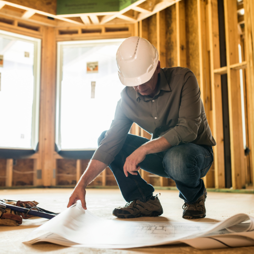 Contractor squatting while reviewing construction plans on-site for a current project.